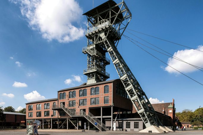 Schiefergruben-Gebäude mit Förderturm vor blauem Himmel und Wolken.