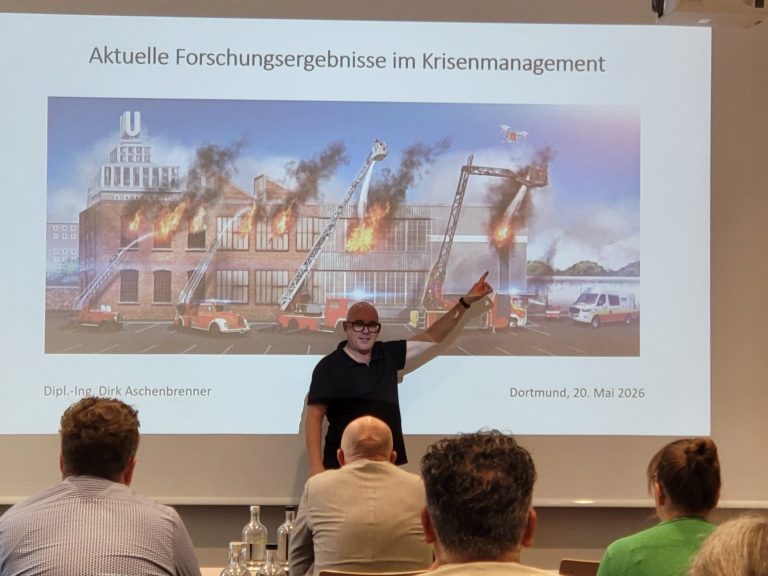 Präsentation über ein brennendes Gebäude mit Feuerwehrleuten und Einsatzfahrzeugen - Dirk Aschenbrenner referiert über Forschungsergebnisse